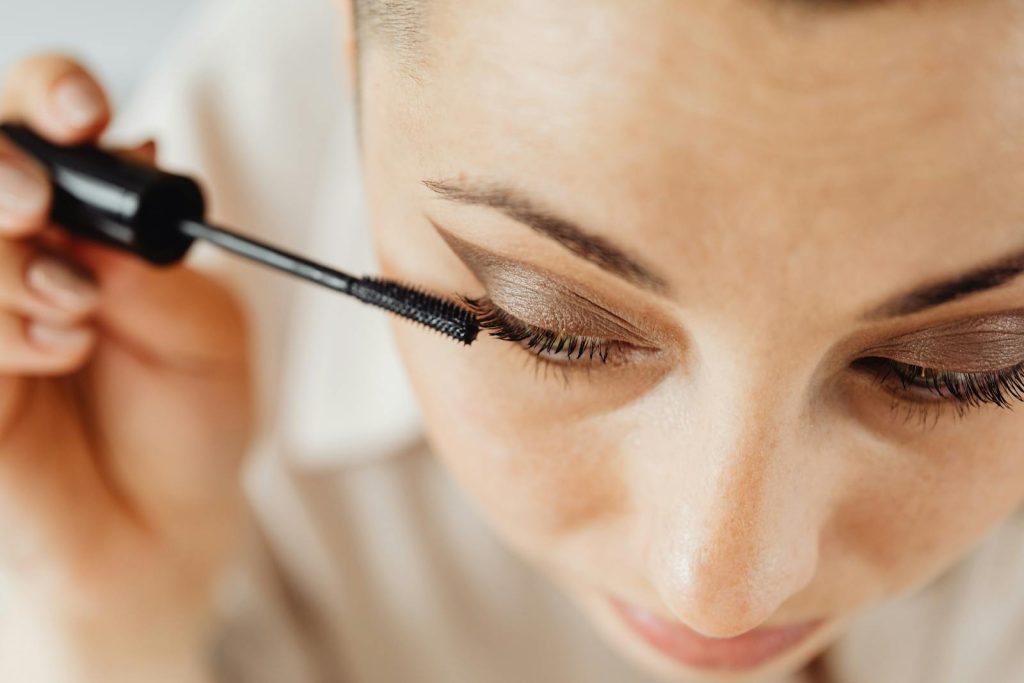 A woman applying mascara to her eyelashes enhances her beauty in a detailed close-up shot.