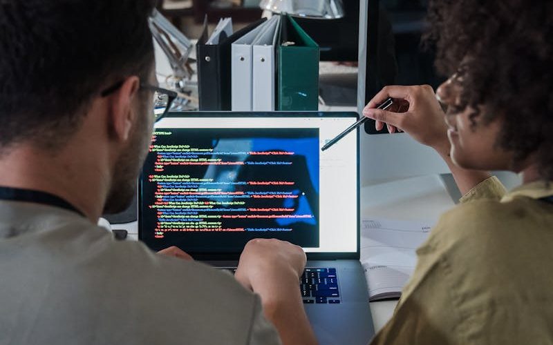 Two developers engage in software programming on a laptop in a modern office setting.